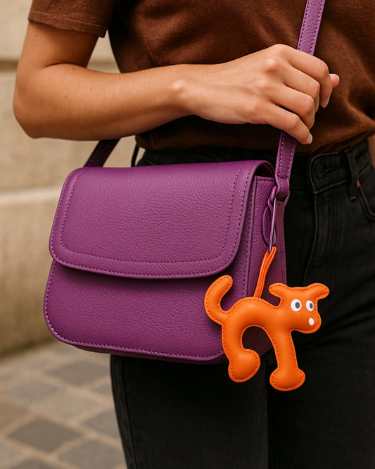 Bijou de sac en forme de chien orange accroché à un sac violet, de la collection LaMartine.
