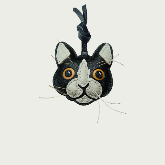Un bijou de sac en cuir représentant une tête de chat et son minois avec moustaches blanches et yeux jaunes.