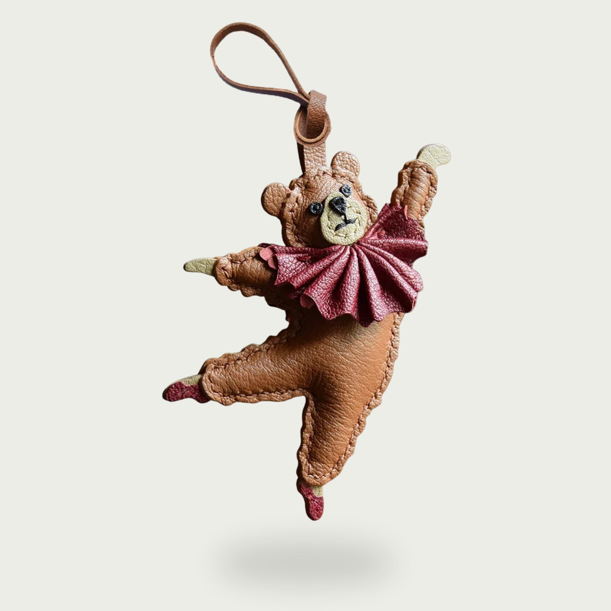 Bijou de sac ou porte-clés en cuir en forme d’ours danseur, bras levés et pieds pointés, sur fond neutre.