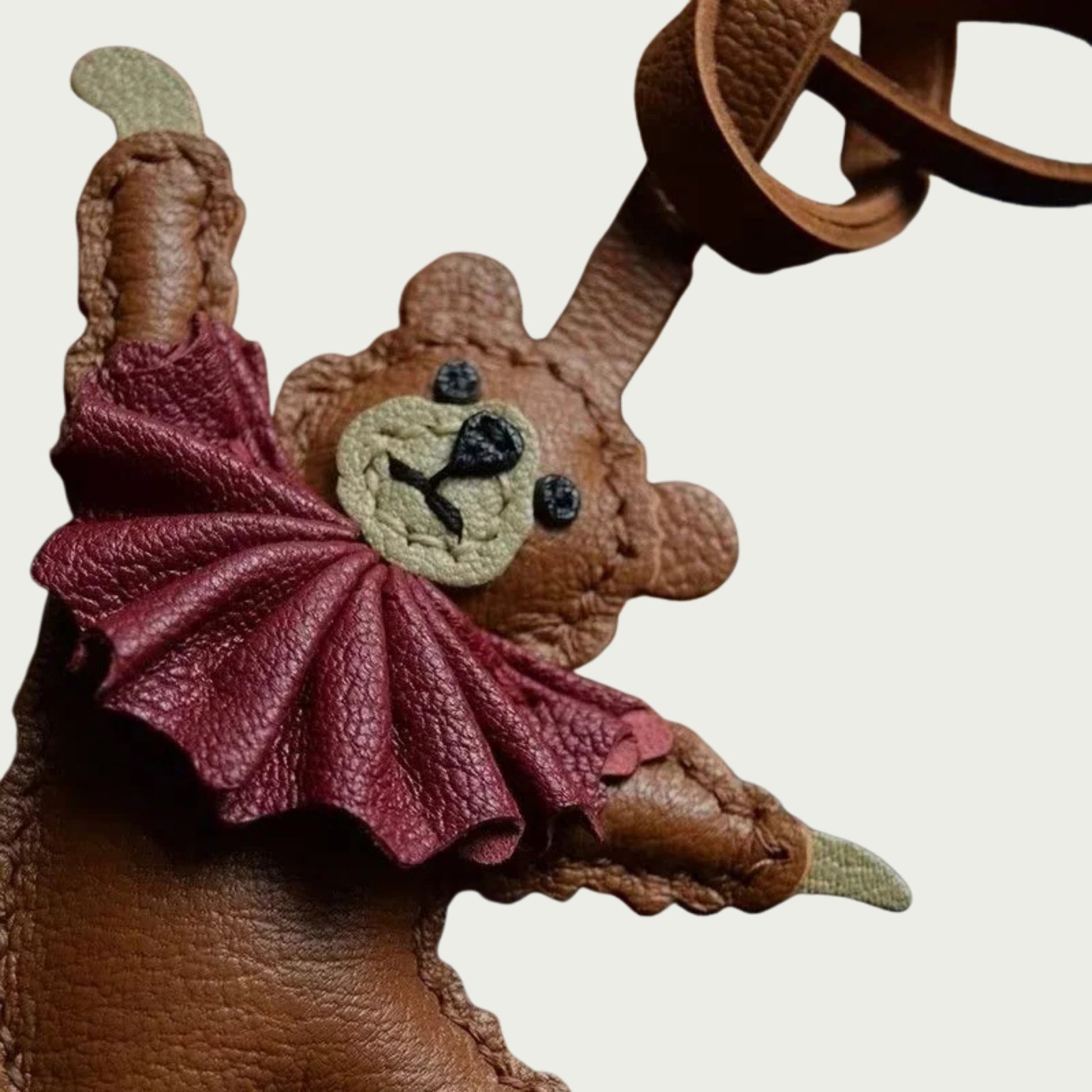 Gros plan sur un bijou de sac en forme d’ours danseur en cuir artisanal, avec collerette lie-de-vin et finitions cousues main.