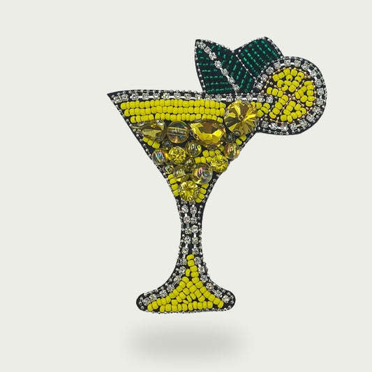 Gros plan sur l’écusson cocktail fait main, brodé de perles jaunes et strass avec cordon de suspension.