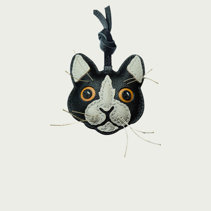 Un bijou de sac en cuir représentant une tête de chat et son minois avec moustaches blanches et yeux jaunes.