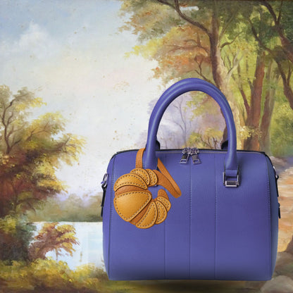 Porte-clés en forme de viennoiserie, grigri en cuir souple rappelant l’élégance artisanale du style parisien.