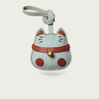 Bijou de sac Maneki-Neko en cuir blanc, avec grelot doré et détails rouges, vu de face sur fond neutre.