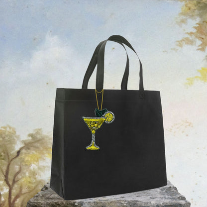 Bijou de sac en forme de cocktail photographié en situation sur un sac, accessoire brodé festif et estival.