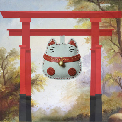 Bijou de sac Maneki-Neko suspendu à un portail torii japonais, dans un décor poétique inspiré de la culture asiatique.