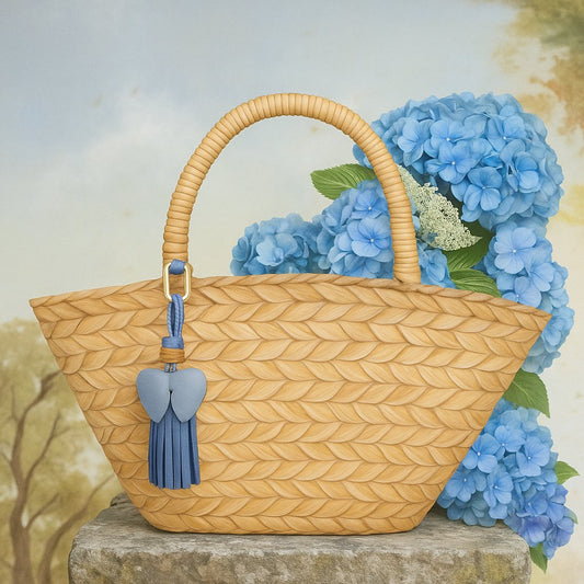 Bijou de sac en cuir Pom-Pom Girl bleu nuit, suspendu à un panier en osier devant des hortensias bleus — accessoire estival LaMartine.