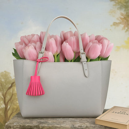 Pompon rose fushia noué sur sac gris avec bouquet de tulipes roses en arrière-plan.