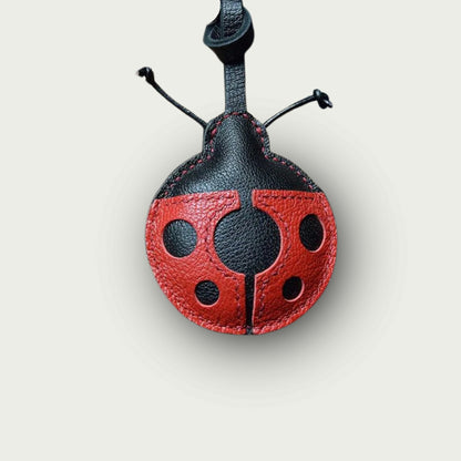 Porte-clés en cuir façonné en coccinelle stylisée, aux ailes rouges à pois noirs, sur fond beige uni, présenté en vue centrée pour une boutique en ligne.